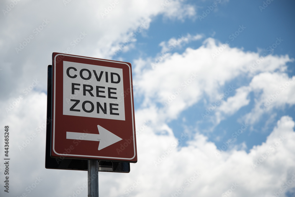 Traffic sign with the text "covid free zone" indicating a zone with vaccinated people or with negative swab. Right arrow. Blue sky and clouds on the background.